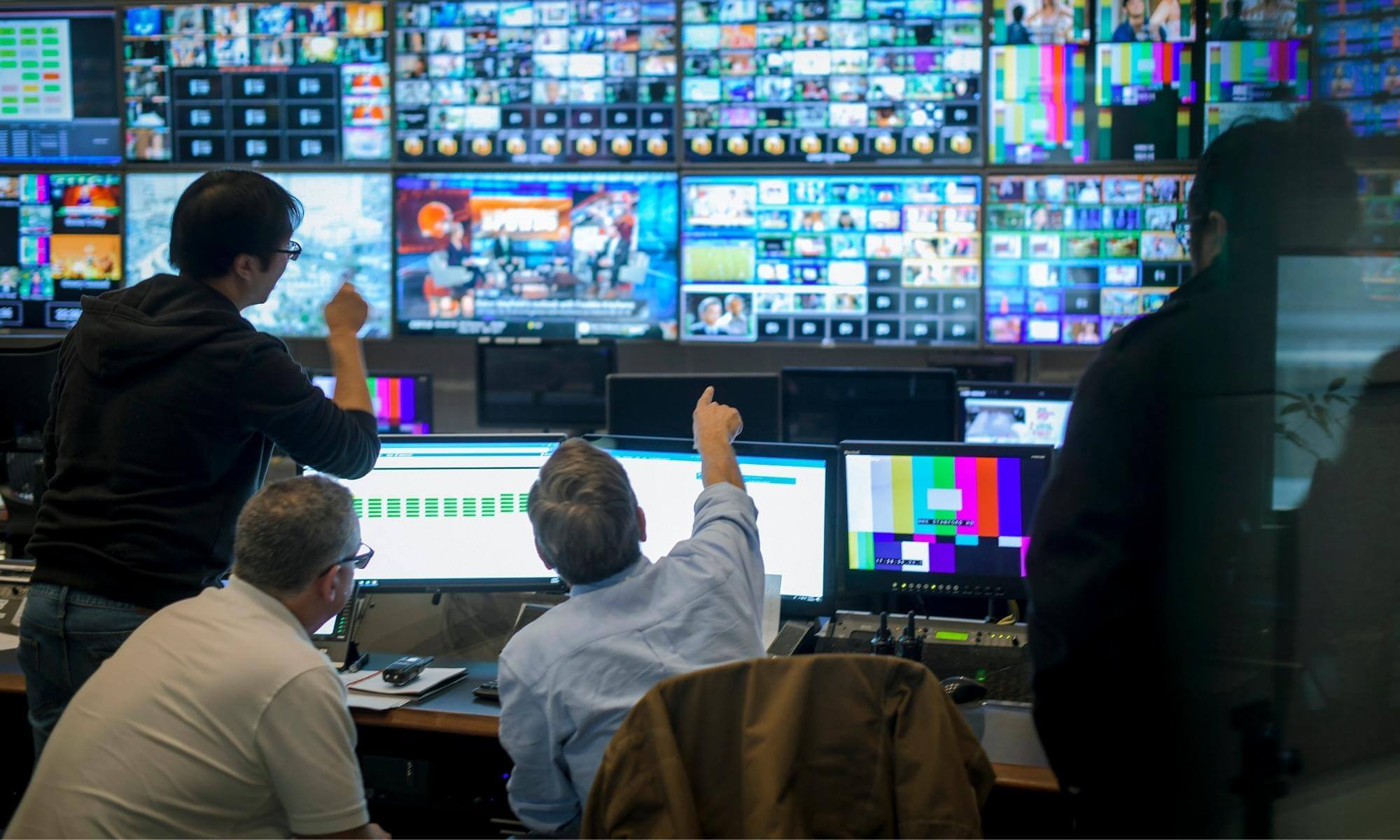 A few employees discussing in front a many large screens on the wall